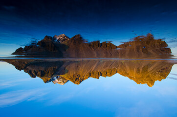 Jagged Vestrahorn Mountain in Iceland during winter with clear sky.  Photo is upside down with reletion in iced over beach.