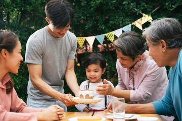 Asian family celebrate birthday party for a kid with cake at yard.