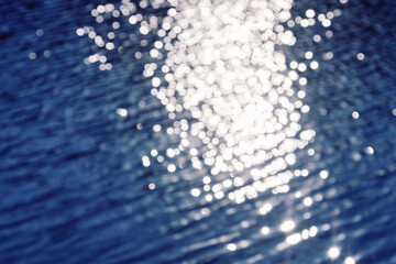 Natural background with blue water surface with path of sunlight reflection. Bokeh pattern texture.