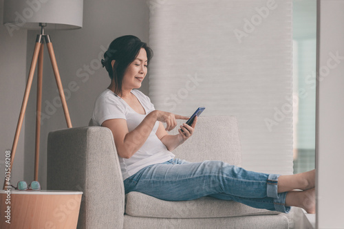 Work from home happy Asian mature woman relaxing in sofa using mobile phone online shopping or remote working.