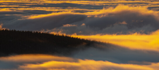 Wall Mural - waves of clouds rolling over the top of the mountain illuminated by the rising sun