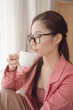 © THESHOTS.CO - Portrait of asian beauty woman wear pink jacket and eyeglasses enjoy cup of coffee.