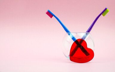 Couple toothbrushes and red heart in glass on pink background with copy space. Family and Valentines Day concept.