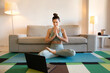 © Wander - Flexible woman doing yoga at home, looking at laptop screen