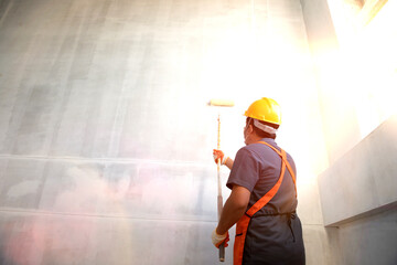 Wall Mural - Room paint job. Asian white room painter with a paint roller in a great hall on a construction site.