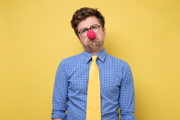 Wall Mural - Sad caucasian man wearing clown red nose on yellow wall.