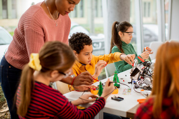 Wall Mural - African American female science teacher with group of kids programming electric toys and robots at robotics classroom