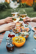 © Przemek Klos - Friends making toast during summer picnic outdoor dinner in a home garden. Close up of people holding wine glasses with white wine over table with pizza, salads and fruits. Dinner in a orchard