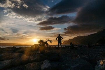 Wall Mural - Silhouette of man over sunset on the sea and mountains background