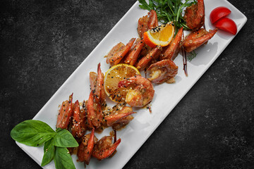 Fried shrimps in garlic-soy sauce, with sesame seeds, on a white plate, on a dark background