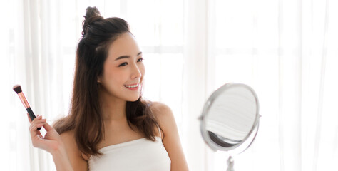 Wall Mural - Smiling of young beautiful pretty woman clean fresh healthy white skin looking at camara.girl holding make-up brushes and make up on face with cosmetics set at home.facial beauty and cosmetic concept