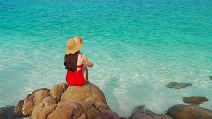 Wall Mural - young woman sitting with arms raised on stone beach with sea at Koh MunNork Island, Rayong, Thailand