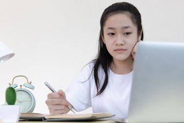 Wall Mural - Asian girl is studying on a laptop and writes in a notebook with intention,Online learning, stay home, New normal, Covid-19 coronavirus, Social distancing, Internet learning...