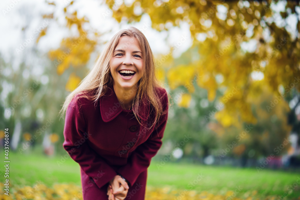Portrait of happy blonde woman in park in autumn. She is enjoying nature. - obrazy, fototapety, plakaty 