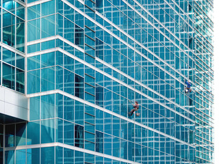 Two industrial climbers with safety tethers wash the glass walls of modern skyscraper. Dangerous work in the metropolis.