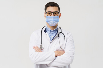 Wall Mural - Portrait of youn doctor wearing surgical mask, holding crossed arms, ready to help patients with coronavirus or covid virus, isolated on gray background