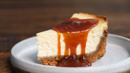 Wall Mural - Slice of cheesecake with caramel sauce, wooden background, closeup view. Salted caramel sauce poured on cheesecake