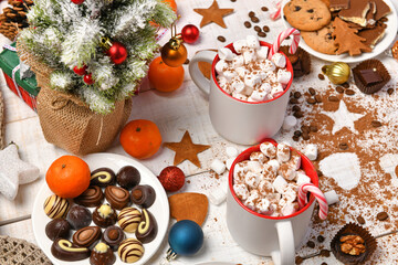 sweet food top view background for merry christmas or new year holiday decoration - chocolate candies, tangerines, cookies, marshmallow and cocoa latte on white wood