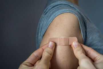a hand putting an adhesive bandage on a woman's arm after injection of vaccine or a scratch on the s