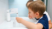 Portrait Of Smiling Little Boy With Mother Washing And Cleaning Dirty Mouth With Water In The Bathroom Sink. Child Washing.