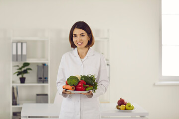 Female nutritionist doctor holds a plate of fresh vegetables in front of her recommending them for diet and weight loss. Concept of a healthy lifestyle and weight loss.