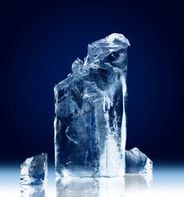 Vertical Rectangular Block Of Ice With A Broken-off Top Isolated On A Dark Blue Background With Clipping Path.
