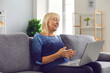 © Studio Romantic - Happy senior woman talking to relatives using video call app on laptop computer sitting on comfortable couch in her apartment. Staying at home, self-isolation and keeping in touch with family concepts
