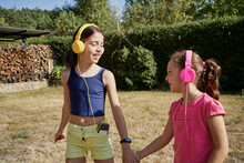 Little girls hugging and listening to music with yellow and pink headphones in the garden. Summer concept