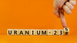 Uranium enrichment symbol. Hand turns cube and changes words 'uranium-238' to 'uranium-235'. Beautiful orange background, copy space. Business, nuclear technology and uranium enrichment concept.