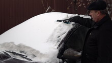 A Man Cleans A Car Windshield From Snow With A Brush. Winter In Russia, The Car Was Covered With Snow