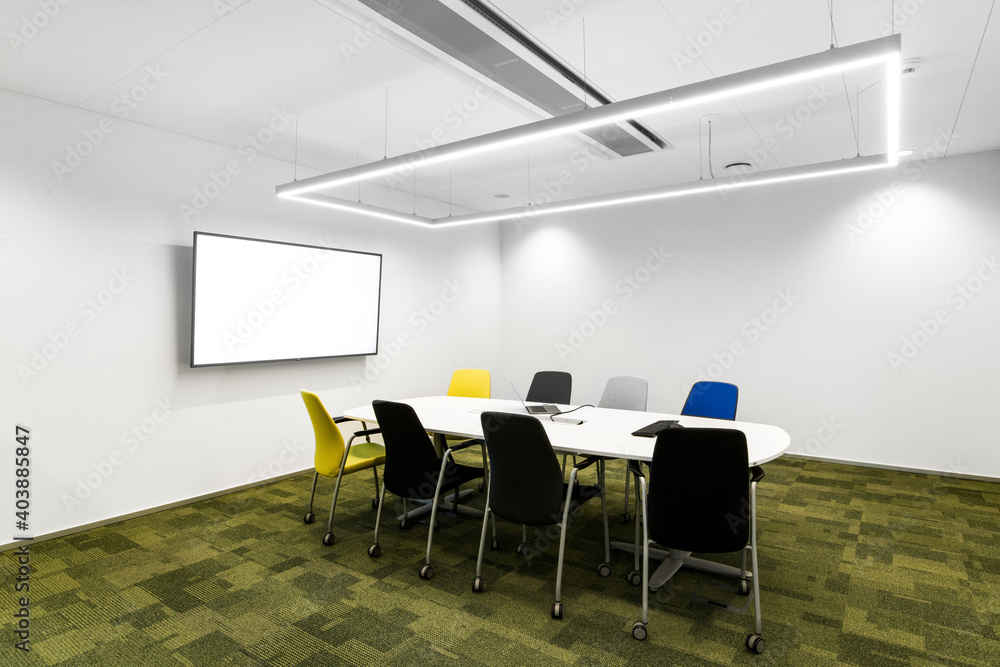 Mała sala konferencyjna w korporacji z monitorem na ścianie, krzesłami, stołem oraz zieloną podłogą - obrazy, fototapety, plakaty 