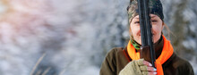 A Young Beautiful Hunter Woman On Hunt In Forest With Rifle On The Shoulder. Winter Season. In The Background Are Snowy Trees. Banner Photo.