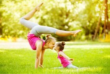 Full Length Of Mother And Daughter Practicing Yoga On Grass