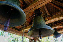 Low Angle Shot Of Old Rusty Bells Hanging From A Wooden Ceiling At Daylight