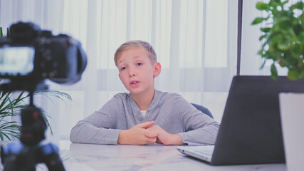 Child blogger videotapes his vlog at home. Boy recording his video blog. White boy speaks in front of a video camera for his blog channel. Little 8 year vlogger makes online streaming using smartphone