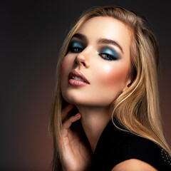 Wall Mural - Portrait of sexy blonde woman with a beautiful face. Fashion model with long hair, studio shot.  Photo of young stylish  woman in black clothes with  blue make-up.