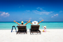 Happy Family On Sunbeds Enjoys Their Vacation On A Tropical Beach With Turquoise Ocean And Sunshine