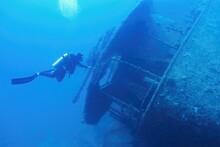 Man Scuba Diver Swimming Near The Ship Wreck In Blue Deep Water. Ship Wreck SS Thistlegormm, Red Sea Egypt.