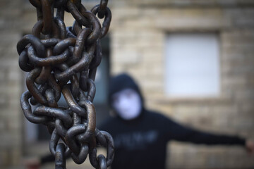 Selective focus shot of an old metal chain and a guy with a mask and hoodie on the background