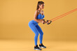 Fitness woman working out with resistance band on orange background. Athletic girl doing exercise