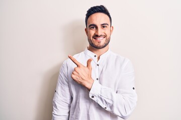 Wall Mural - Young handsome man with beard wearing casual t-shirt standing over white background smiling cheerful pointing with hand and finger up to the side