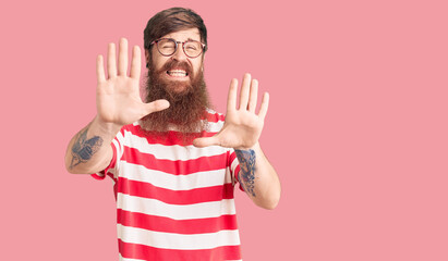 Canvas Print - Handsome young red head man with long beard wearing casual clothes afraid and terrified with fear expression stop gesture with hands, shouting in shock. panic concept.