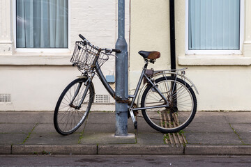 An old ladies bike with a basket chained to a lamppost in the street