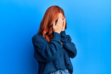 Poster - Young beautiful redhead woman wearing casual sweater and glasses over blue background with sad expression covering face with hands while crying. depression concept.