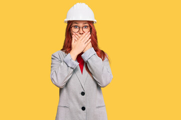 Canvas Print - Young redhead woman wearing architect hardhat shocked covering mouth with hands for mistake. secret concept.