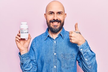 Sticker - Young handsome man holding pills smiling happy and positive, thumb up doing excellent and approval sign