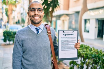 Poster - Young african american businessman smiling happy holding clipboard with agreement document at the city.