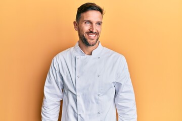 Sticker - Handsome man with beard wearing professional cook uniform looking away to side with smile on face, natural expression. laughing confident.