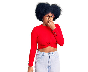 Sticker - Young african american girl wearing casual clothes and glasses smelling something stinky and disgusting, intolerable smell, holding breath with fingers on nose. bad smell