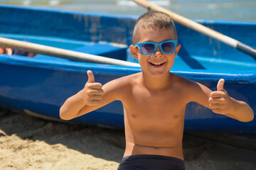 Canvas Print - A young boy in a blue boat on the ocean. A child in sunglasses on the beach near the shore.